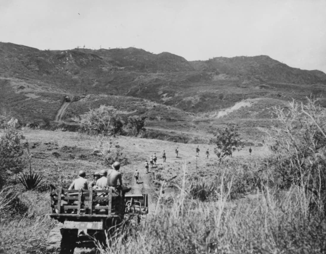 A marine tractor, loaded with ammunition and water, follows marines along a road leading to the front lines on Guam, July 1944