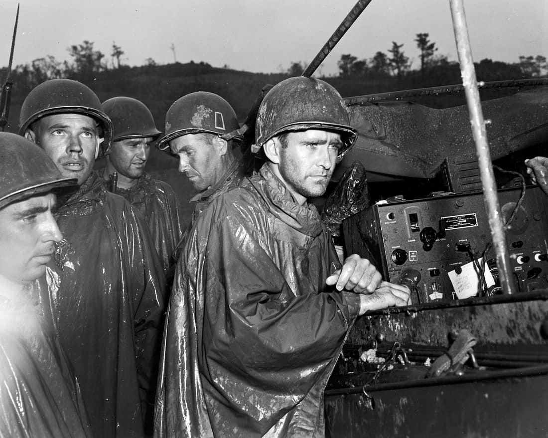 A few yards behind the front lines on Okinawa, fighting men of the US Armys 77th Infantry division listen to radio reports of Germanys surrender on May 8, 1945. Their battle hardened faces indicate the impassiveness with