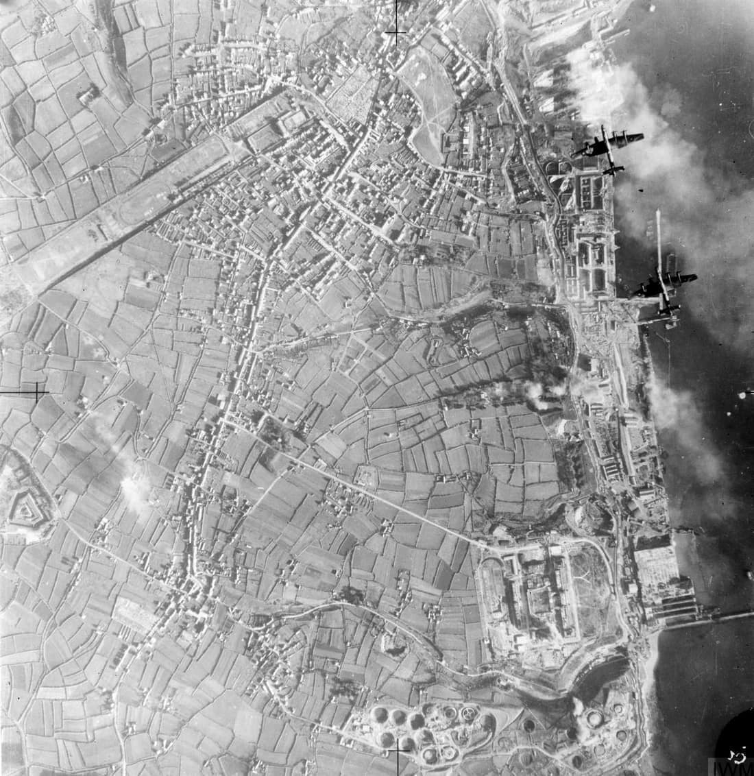 Royal Air Force Bomber Command, 1939-1941. Vertical aerial photograph taken during a daylight attack on German warships docked at Brest, France. Two Handley Page Halifaxes of No. 35 Squadron RAF (upper right) fly over th