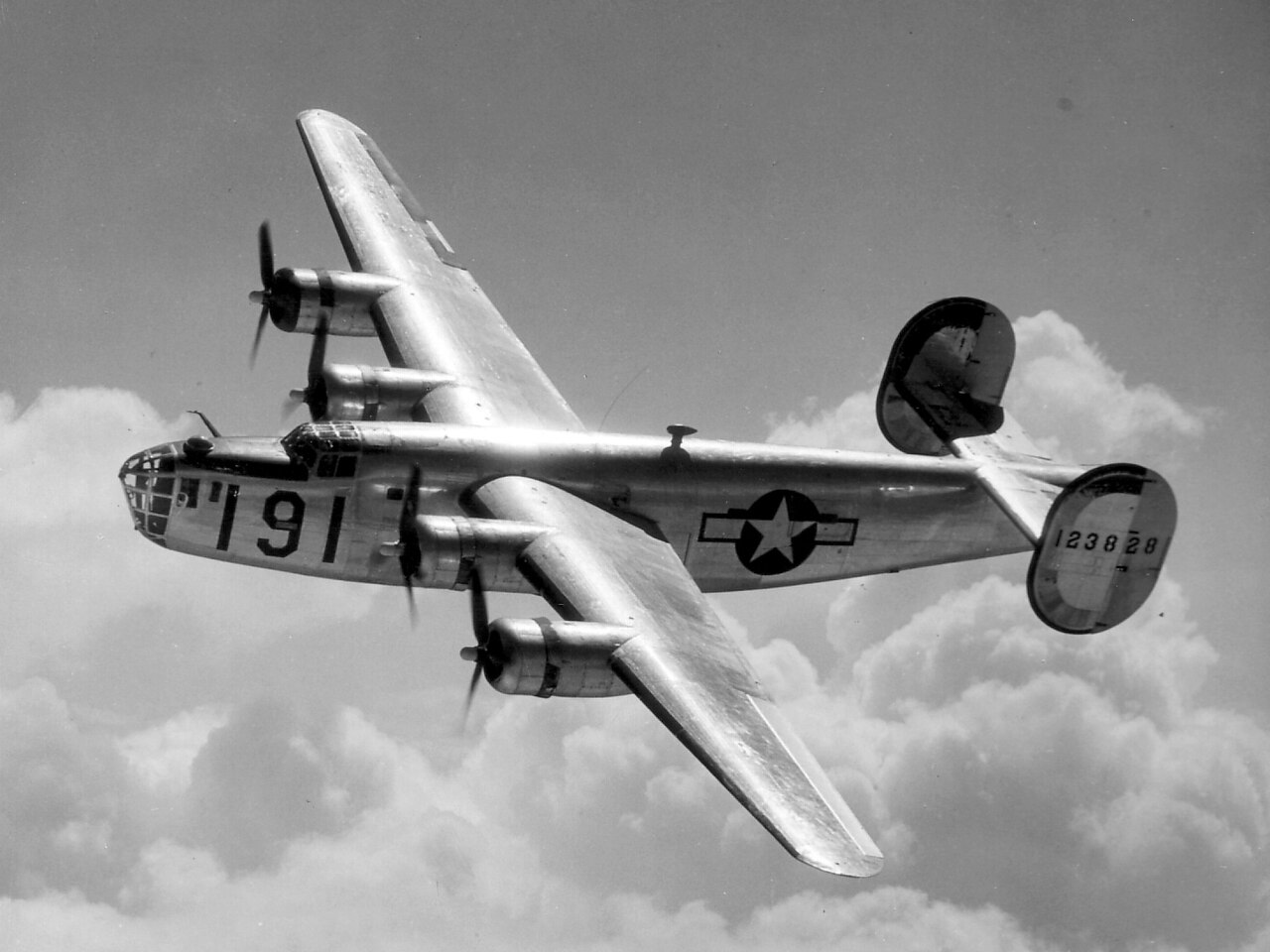 A Consolidated B-24 Liberator from Maxwell Field, Alabama, four engine pilot school, glistens in the sun as it makes a turn at high altitude in the clouds. The B-24 is B-24D-7-CO 41-23828, which was later assigned to the
