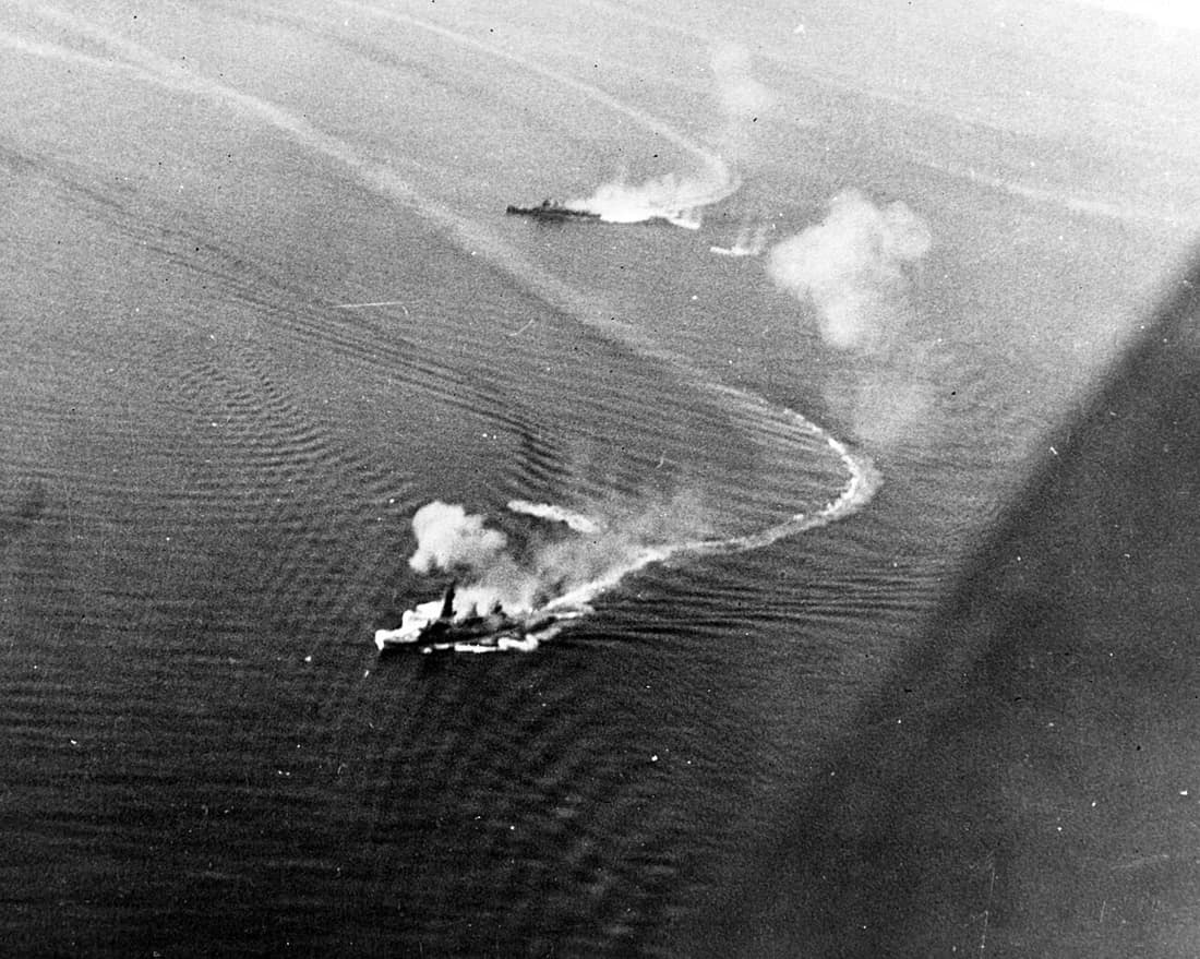 Imperial Japanese Navy battleship Fusō (foreground) under air attack by United States Navy carrier aircraft hours before the Battle of Surigao Strait during the Battle of Leyte Gulf. Fusō was damaged by several bomb hits
