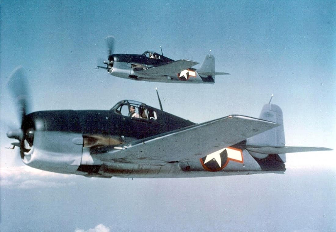 Two U.S. Navy Grumman F6F-3 Hellcats in tricolor camouflage, sea blue, intermediate blue, and insignia white.
