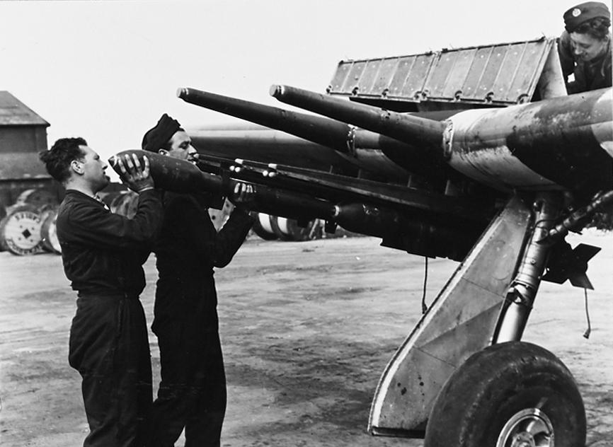 3 in, 60 pdr SAP, Rocket Projectiles being loaded onto the launch rails of an RAF Hawker Typhoon, circa 1944. A pair of 20mm cannon barrels are visible above the launch rails.