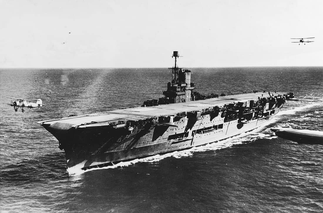 The British Royal Navy aircraft carrier HMS Ark Royal (91) photographed circa 1939. A Fairey Swordfish aircraft is taking off as another approaches from astern. Two are visible in the background.
