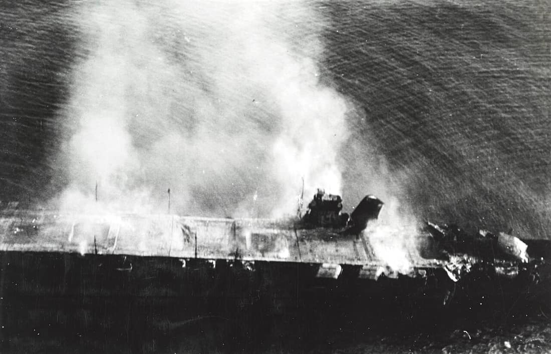 The burning Japanese aircraft carrier Hiryu, photographed by a Yokosuka B4Y aircraft from the carrier Hosho shortly after sunrise on 5 June 1942. Hiryu sank a few hours later. Note collapsed flight deck at right. Part of