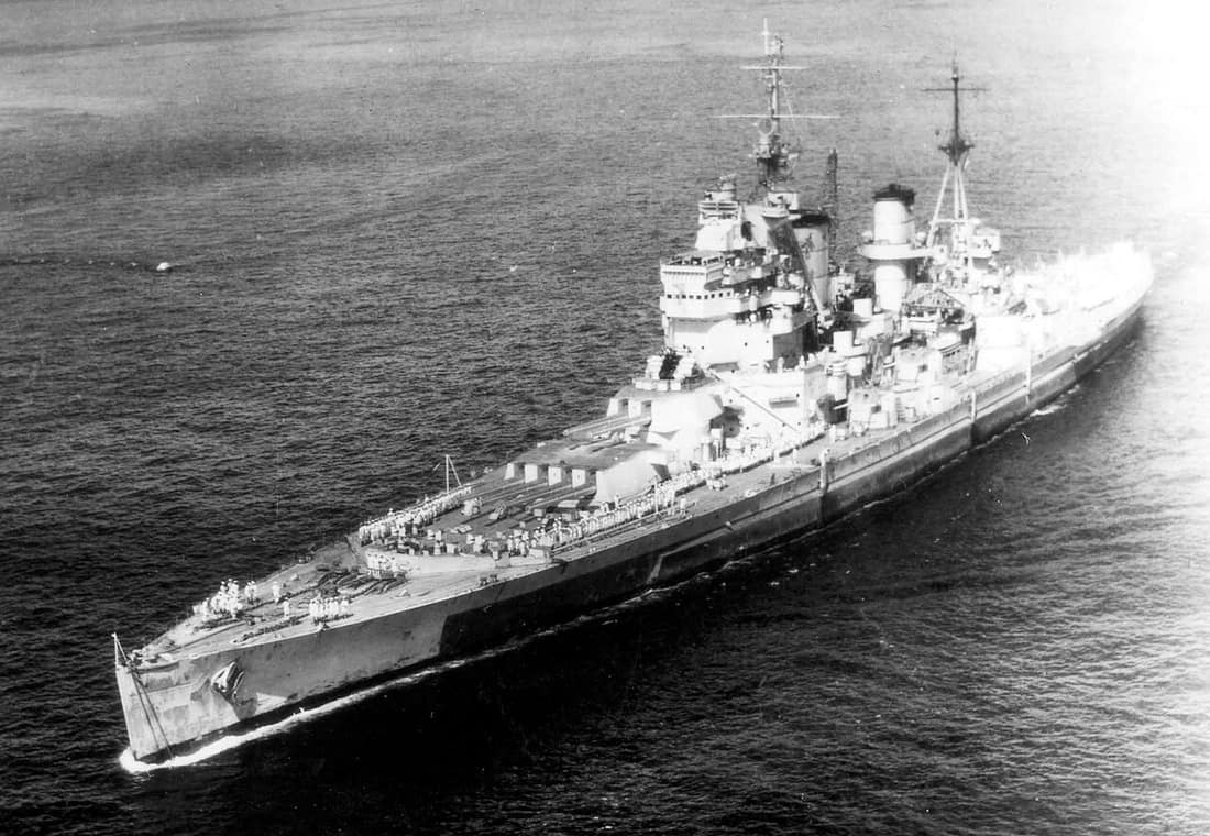 The British battleship HMS King George V enters Apra Harbor, Guam, with sailors in formation on deck. 1945