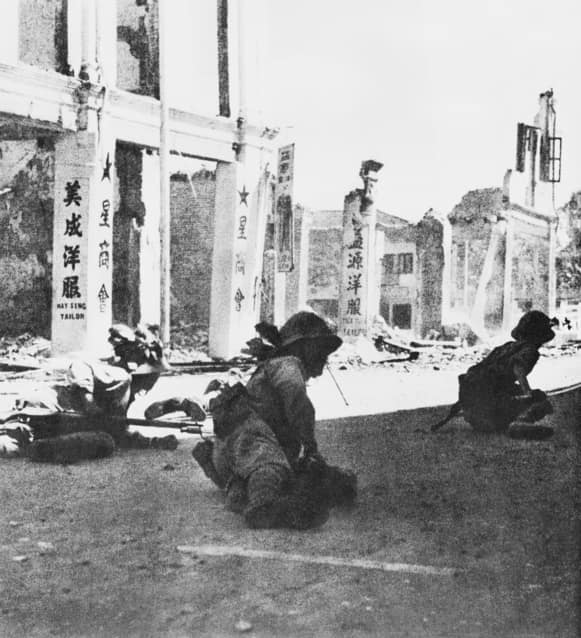 JAPANESE TROOPS CROUCH LOW IN THE STREET DURING THE FINAL STAGES OF THEIR INVASION OF THE MALAYAN PENINSULA WHICH CULMINATED IN THE SURRENDER OF ALL BRITISH FORCES, AND THE OCCUPATION OF THE BRITISH NAVAL BASE ON SINGAPO