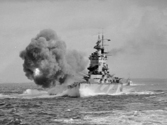 HMS Nelson firing her 16-inch guns during a practice shoot of gunnery trials and exercises after her repair. Note how the massive muzzle blast churns up the water to starboard.