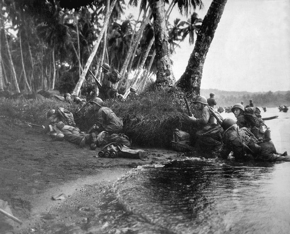 Landing operations on Rendova Island, Solomon Islands, 30 June 1943. Attacking at the break of day in a heavy rainstorm, the first Americans ashore huddle behind tree trunks and any other cover they can find. (Navy) NARA
