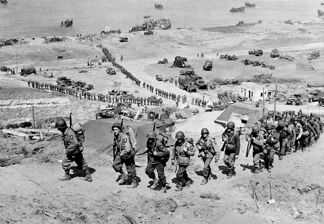 Troops of the US Army 2nd Infantry Division march up the bluff at the E-1 draw in the Easy Red sector of Omaha Beach, Normandy, France on D+1, June 7, 1944. They are going past the German bunker, Widerstandsnest 65 (WN 6