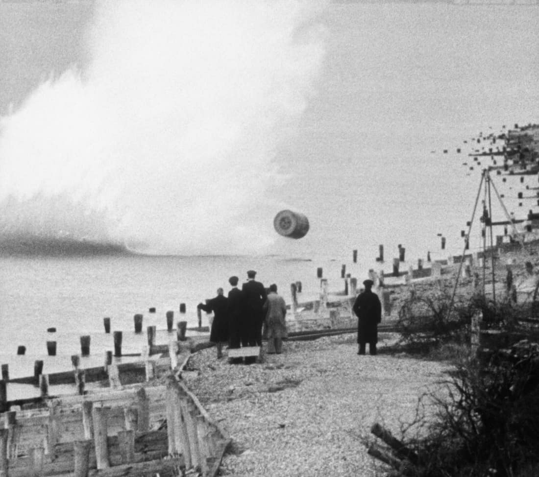Movie still, showing an inert, practice version of the Upkeep bouncing bomb being dropped during a training flight by members of RAF 617 Squadron at Reculver bombing range, Kent. The bomb's designer, Barnes Wallis, and o