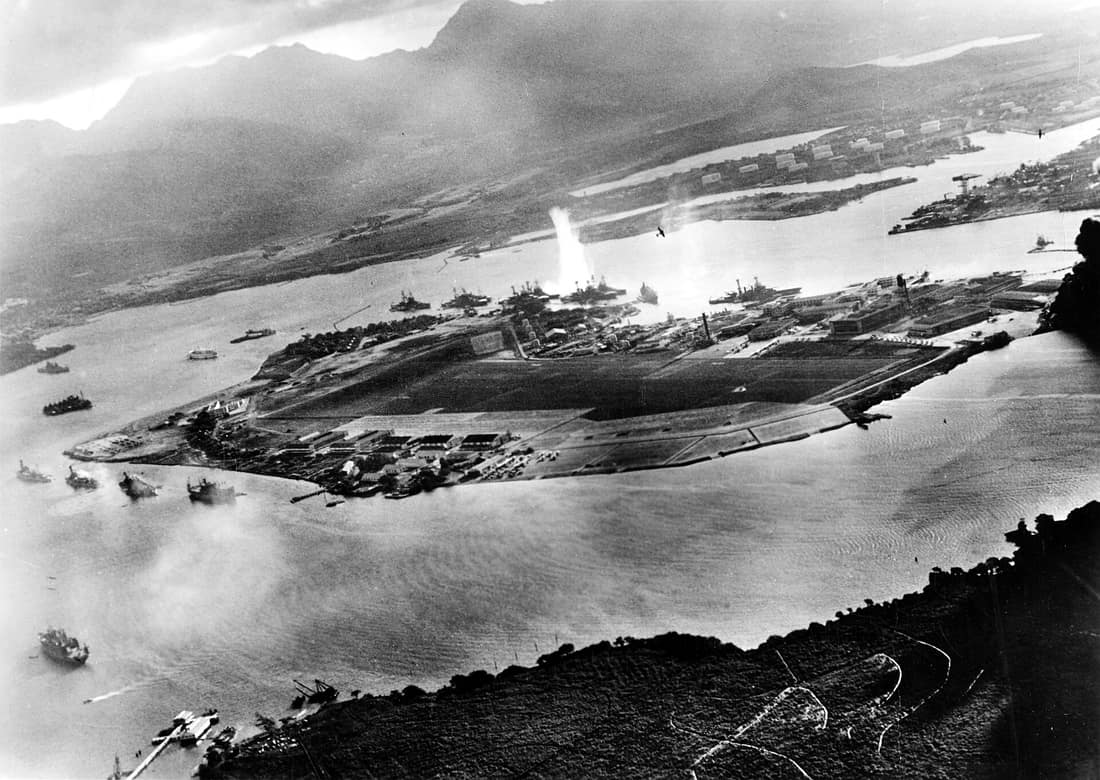 Photograph taken from a Japanese plane during the torpedo attack on ships moored on both sides of Ford Island shortly after the beginning of the Pearl Harbor attack. View looks about east, with the supply depot, submarin