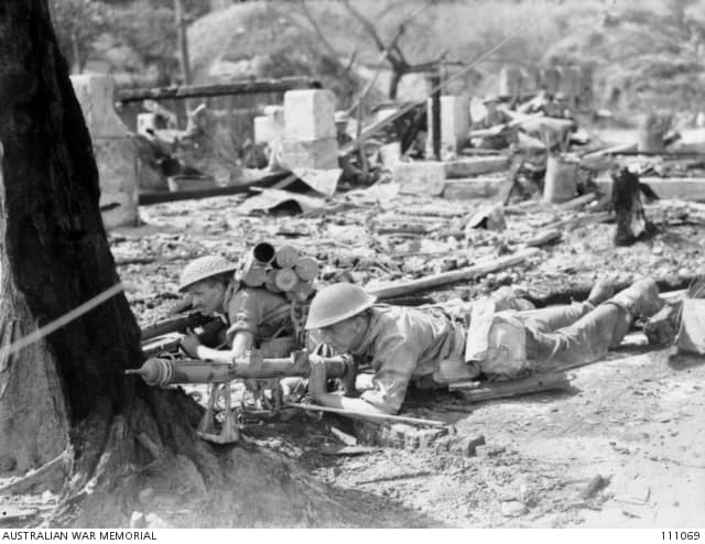 IWM caption : SX27501 Private (Pte) Aubrey Carl Kotz (left) and Pte W Spence (right), members of 7 Platoon, A Company, 2/10 Battalion take cover behind a tree in the town area with their PIAT (Projector, Infantry, Anti T