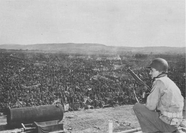 At a prisoner-of-war enclosure near Remagen, Germany, one of the Rheinwiesenlager, a U.S. soldier takes part in keeping guard over thousands of German soldiers captured in the Ruhr area.