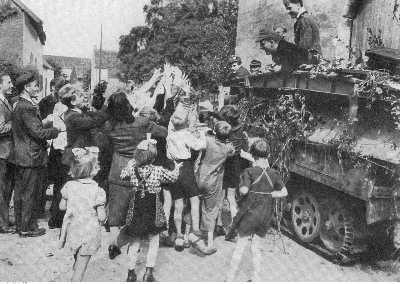 Niemiecki wóz pancerny Sd Kfz 251/7 Ausf D w miejscowości na zachodzie Niemiec witany przez ludność. Żołnierze rzucają dzieciom cukierki.
