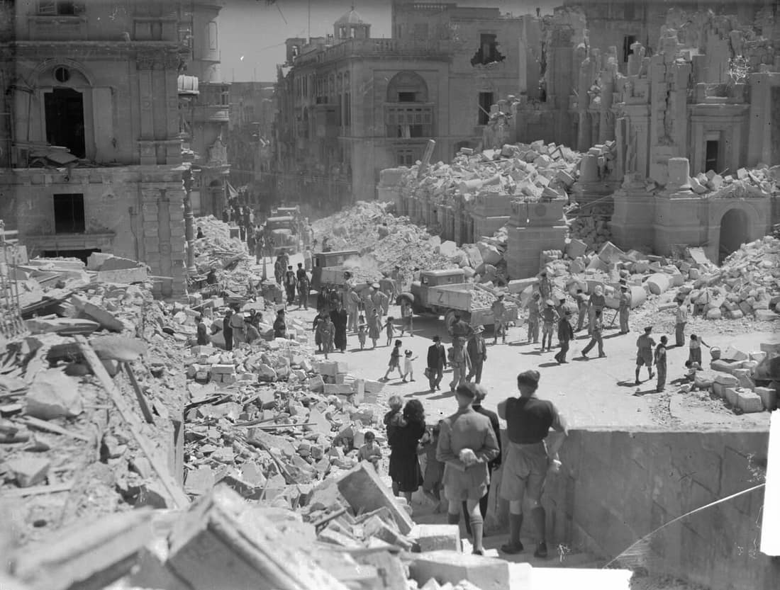 A heavily bomb-damaged street in Valletta, Malta. This street is Kingsway, the principal street in Valetta. Service personnel and civilians are present clearing up the debris.