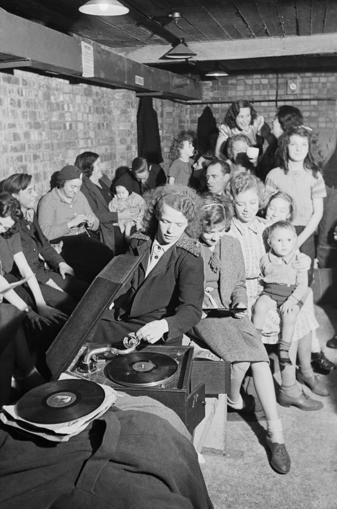 A young woman plays a gramophone in an air raid shelter in north London during 1940. A young woman places the gramophone needle on a record to bring some light relief to an air raid shelter, somewhere in north London. Th