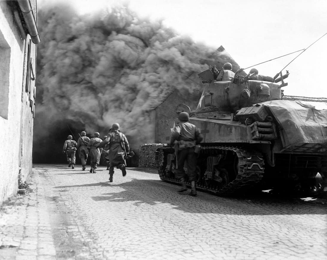 Soldiers of the 55th Armored Infantry Battalion and tank of the 22nd Tank Battalion, 11 Armored Division, move through smoke filled street. Wernberg, Germany.